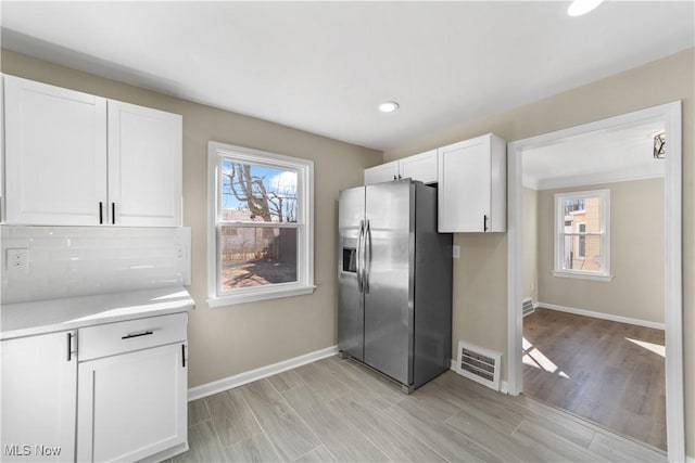 kitchen featuring tasteful backsplash, visible vents, stainless steel fridge, and white cabinets