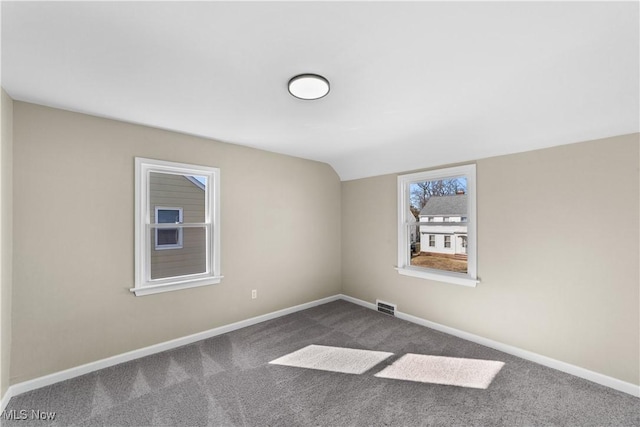 empty room featuring visible vents, dark carpet, baseboards, and vaulted ceiling