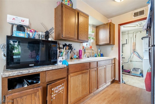 kitchen featuring visible vents, light wood-style flooring, a sink, light countertops, and black microwave