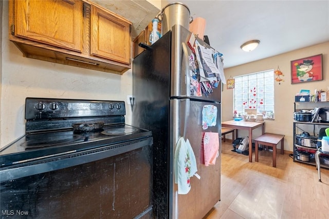 kitchen with brown cabinetry, light wood-style flooring, freestanding refrigerator, and black electric range