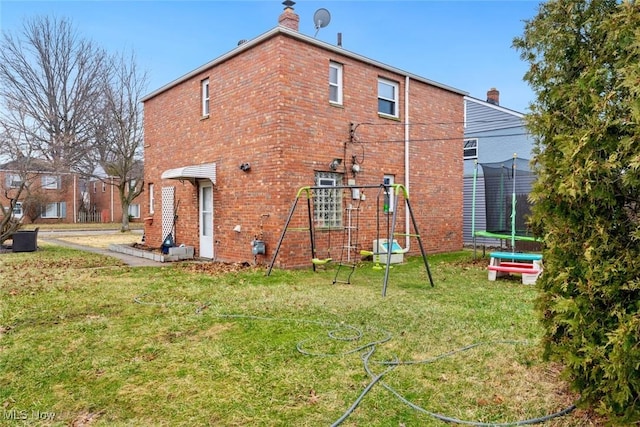 back of property featuring a trampoline, a lawn, brick siding, and a chimney