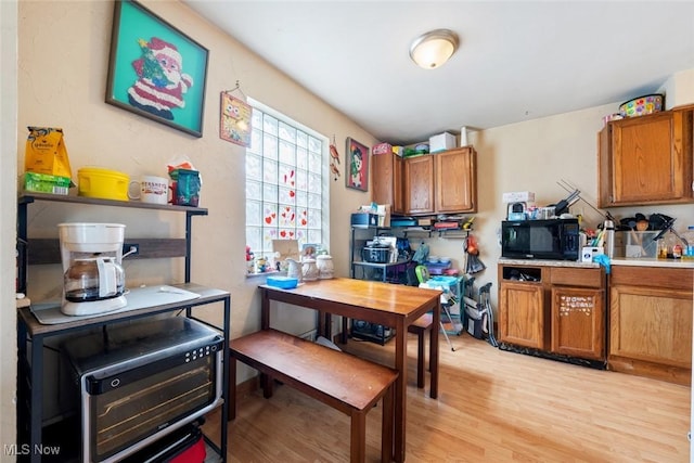 kitchen with brown cabinetry, light countertops, light wood-type flooring, and black microwave