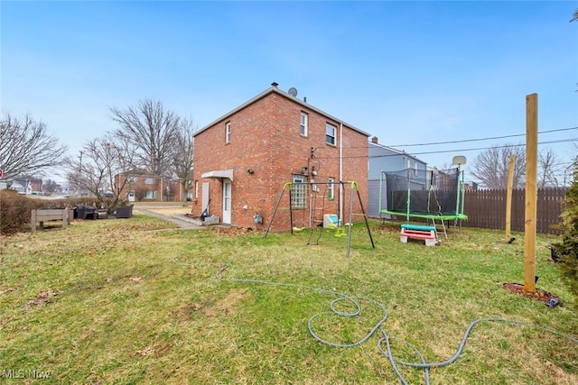 rear view of property with brick siding, a playground, a trampoline, fence, and a lawn