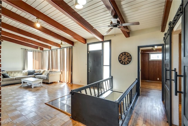 living area featuring vaulted ceiling with beams, baseboards, a barn door, wood finished floors, and a ceiling fan