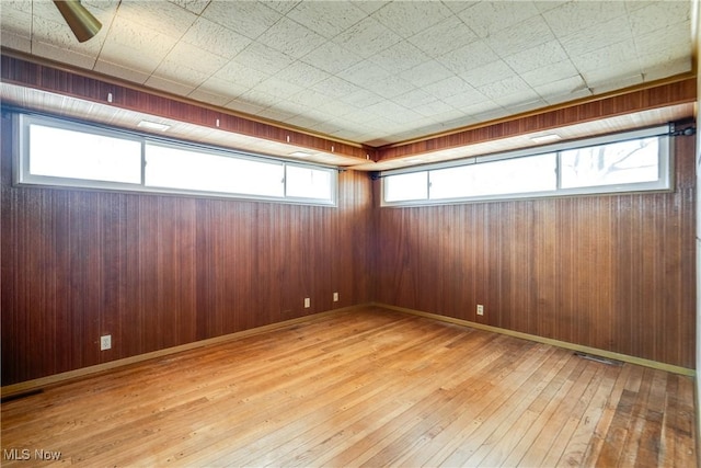 unfurnished room with light wood-style flooring, wooden walls, and baseboards