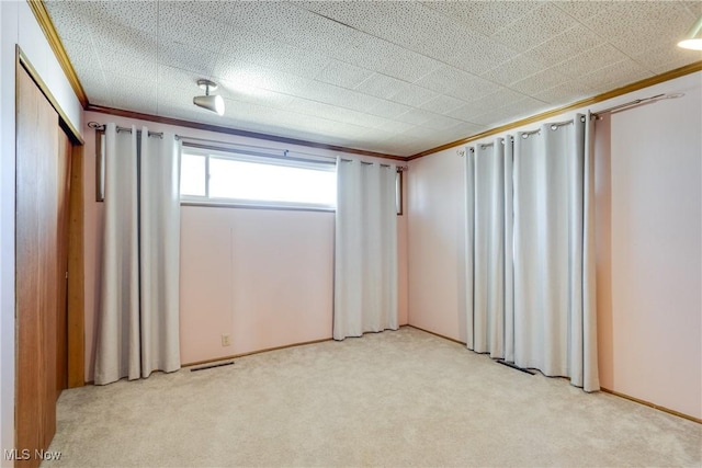 spare room featuring visible vents, light colored carpet, crown molding, and baseboards