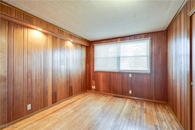 empty room with visible vents, baseboards, light wood-style floors, and wood walls