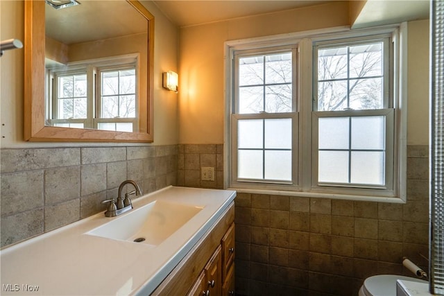 half bath with vanity, tile walls, toilet, and wainscoting