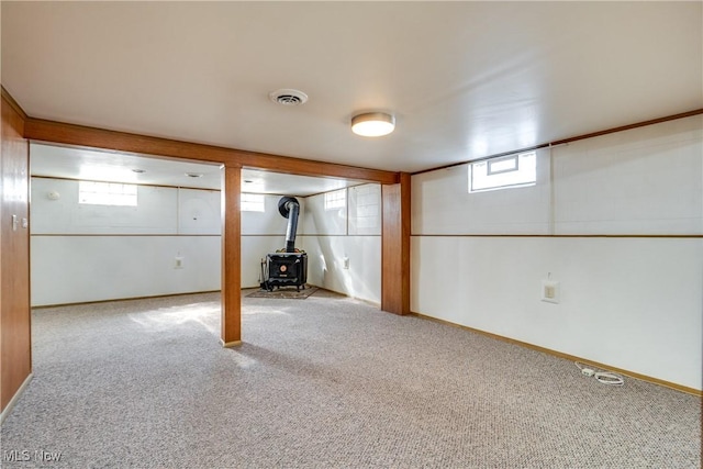 below grade area featuring a wood stove, carpet flooring, baseboards, and visible vents