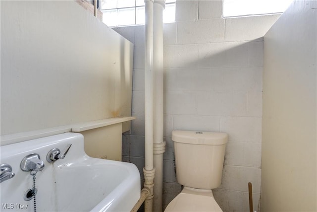 half bath featuring a sink, toilet, and concrete block wall