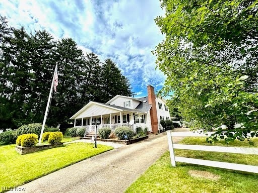 view of front facade featuring a front lawn, covered porch, driveway, and a chimney