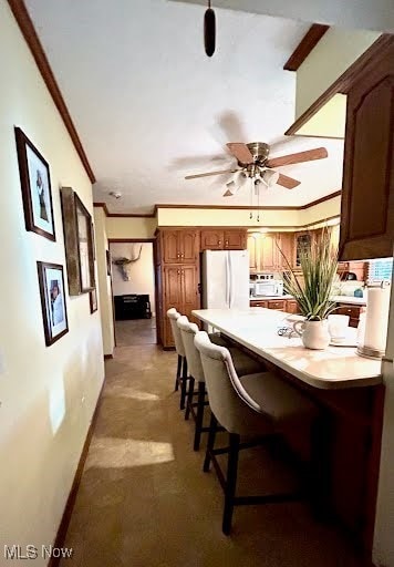 interior space featuring a peninsula, freestanding refrigerator, light countertops, crown molding, and a kitchen breakfast bar