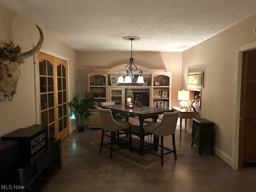 dining area with a textured ceiling, french doors, baseboards, and a chandelier