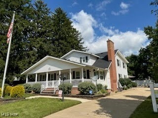 view of front of house with covered porch, driveway, a chimney, and a front yard