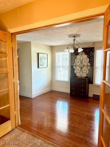 unfurnished dining area with a notable chandelier, a textured ceiling, baseboards, and wood finished floors