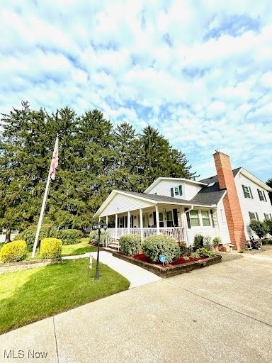 view of front of home featuring a chimney, a front lawn, a porch, and driveway