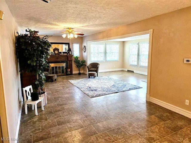 interior space with baseboards, a textured ceiling, a glass covered fireplace, and a ceiling fan