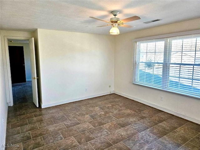 spare room with visible vents, stone finish floor, a ceiling fan, and baseboards