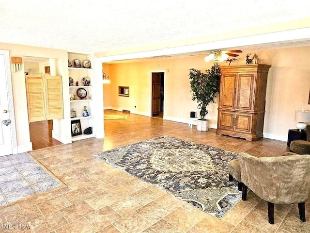 living area with ceiling fan, built in shelves, baseboards, and stone finish flooring