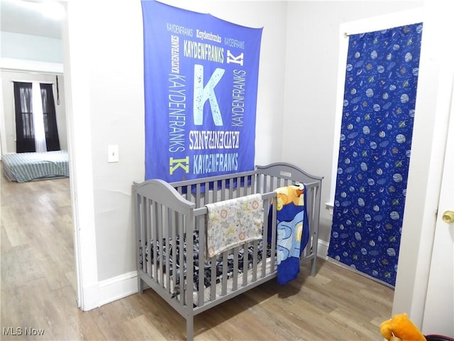 bedroom with baseboards, a nursery area, and wood finished floors