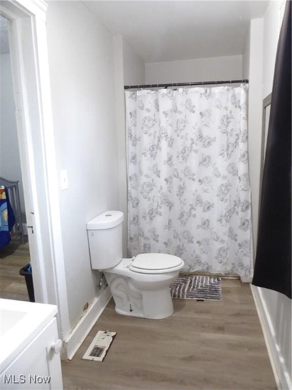 bathroom with visible vents, toilet, wood finished floors, a shower with shower curtain, and vanity