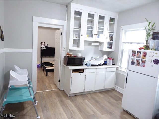 kitchen with freestanding refrigerator, light countertops, black microwave, white cabinetry, and light wood-type flooring