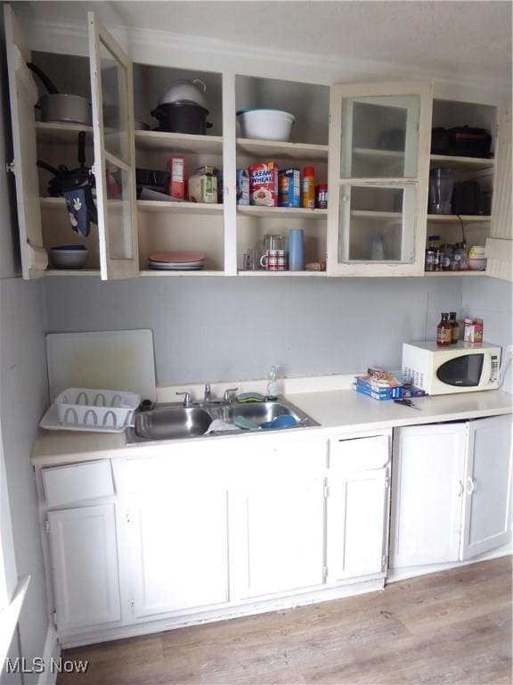 kitchen with white microwave, white cabinetry, light wood-style floors, and a sink