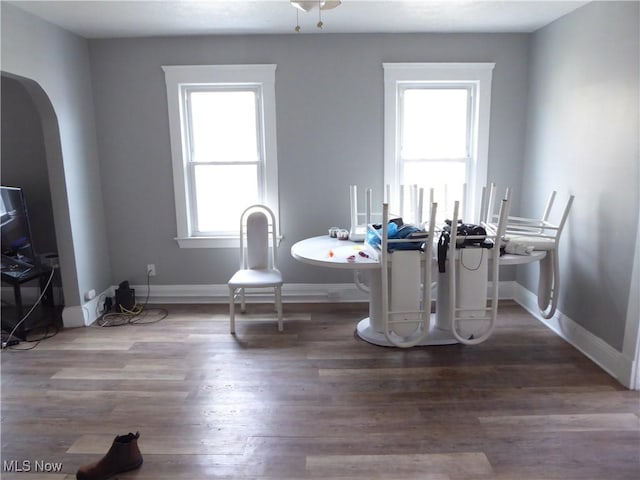 dining space featuring wood finished floors, arched walkways, and baseboards