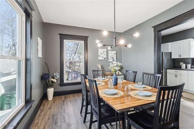 dining space with baseboards, a notable chandelier, and light wood finished floors