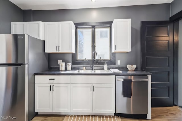 kitchen featuring light wood-style flooring, a sink, stainless steel appliances, white cabinetry, and dark countertops