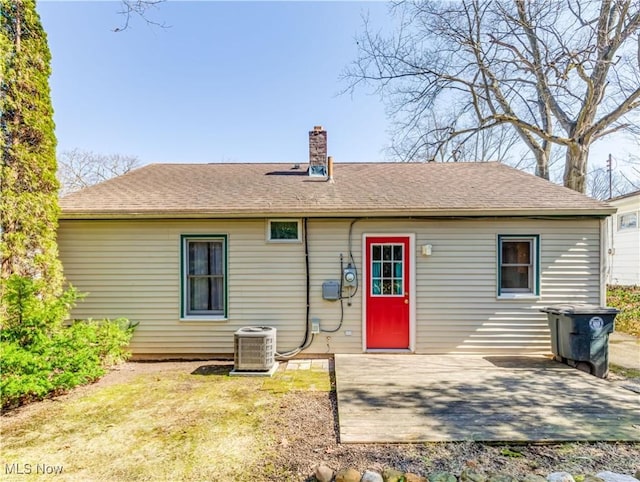 rear view of house featuring a shingled roof, cooling unit, a patio area, and a chimney