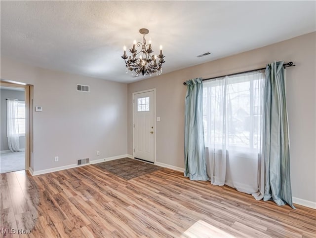 entrance foyer with light wood finished floors, visible vents, baseboards, an inviting chandelier, and a textured ceiling