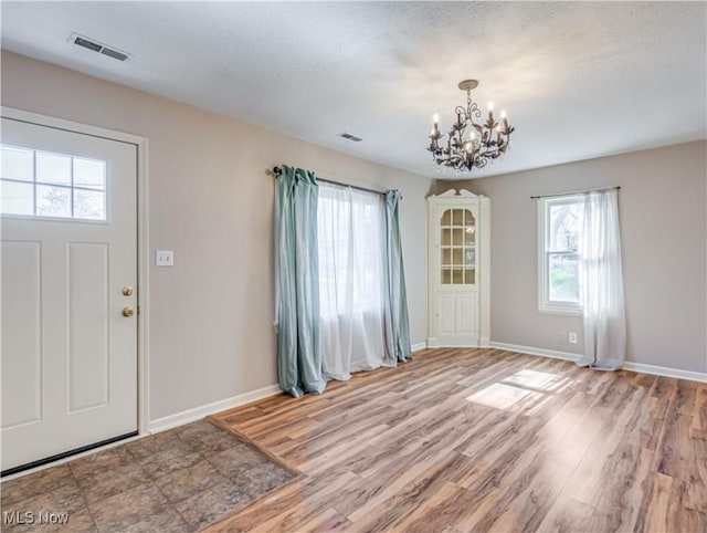 entryway featuring visible vents, an inviting chandelier, baseboards, and light wood-style floors