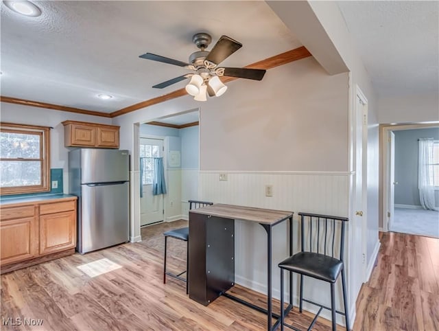 kitchen with crown molding, light wood-style floors, freestanding refrigerator, and wainscoting