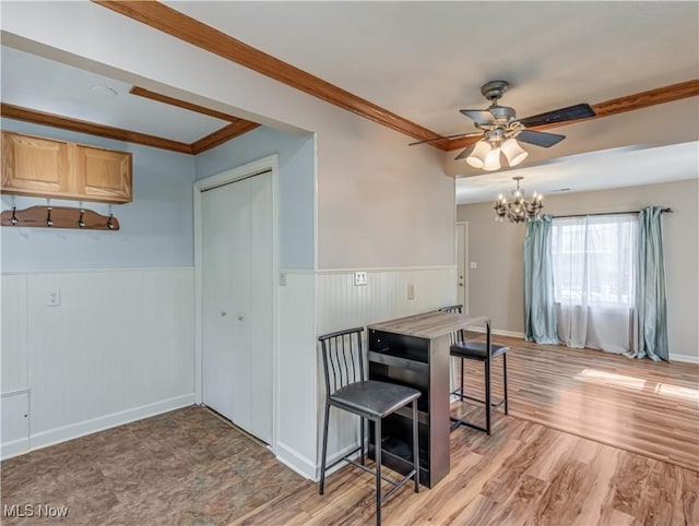 interior space with ceiling fan with notable chandelier, crown molding, wainscoting, and light wood finished floors