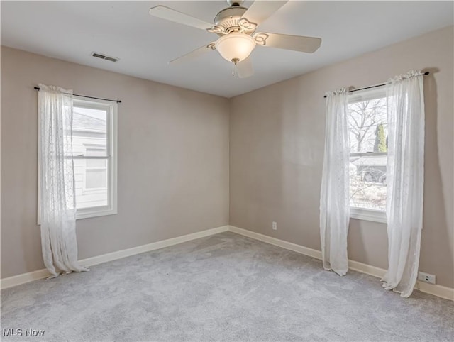 carpeted spare room featuring baseboards, visible vents, and ceiling fan