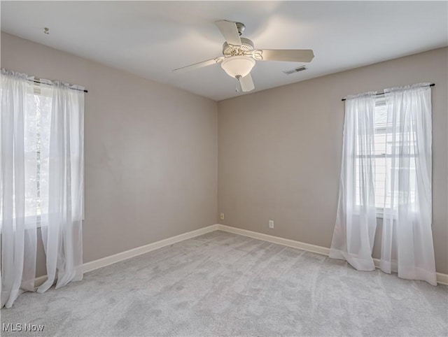 unfurnished room with a ceiling fan, visible vents, light colored carpet, and baseboards