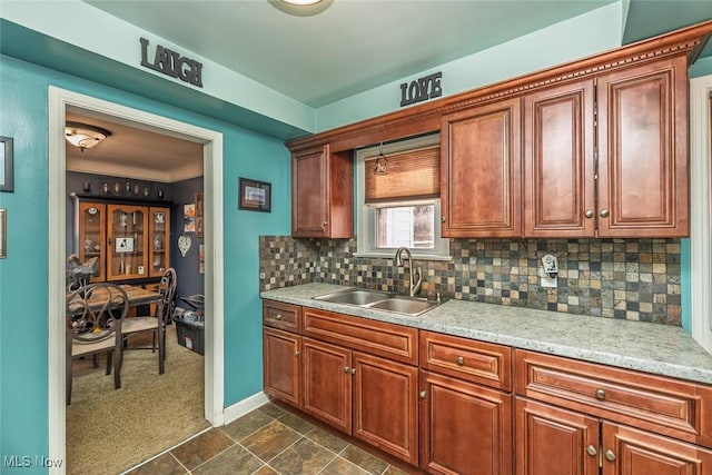 kitchen with brown cabinets, a sink, tasteful backsplash, dark colored carpet, and baseboards