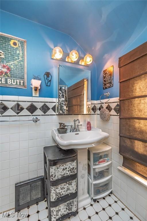 bathroom featuring a wainscoted wall, visible vents, lofted ceiling, a sink, and tile walls