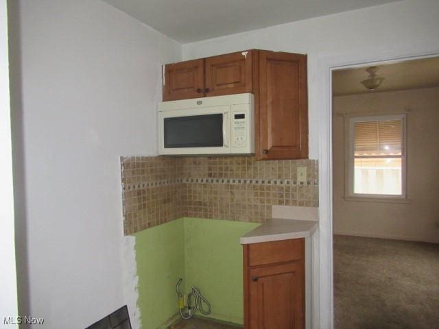 kitchen with brown cabinetry, white microwave, carpet floors, decorative backsplash, and light countertops