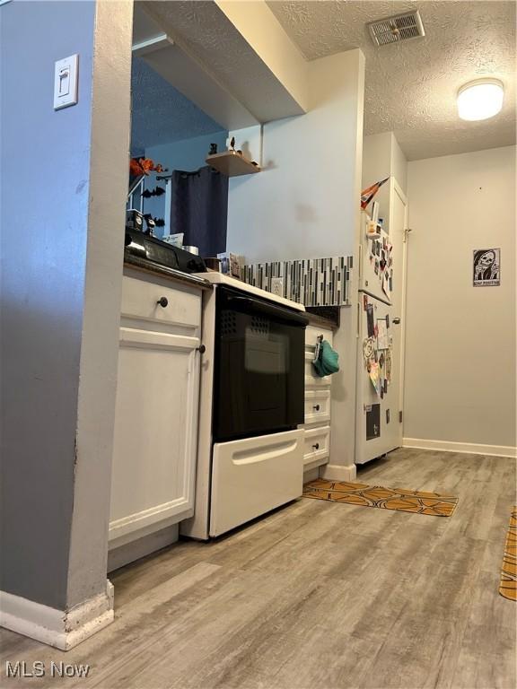 kitchen with visible vents, baseboards, light wood-style floors, white cabinets, and a textured ceiling