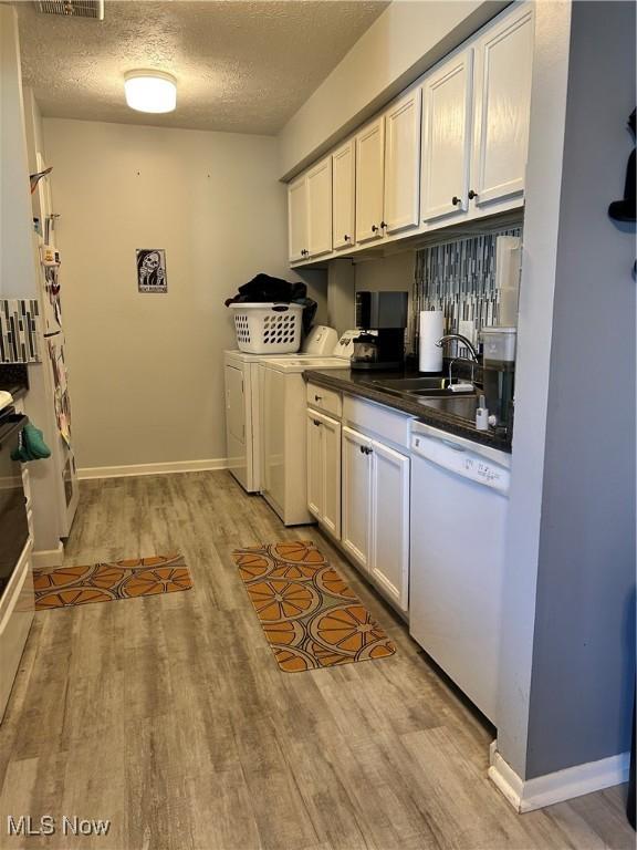 clothes washing area with independent washer and dryer, a sink, a textured ceiling, light wood-style floors, and laundry area