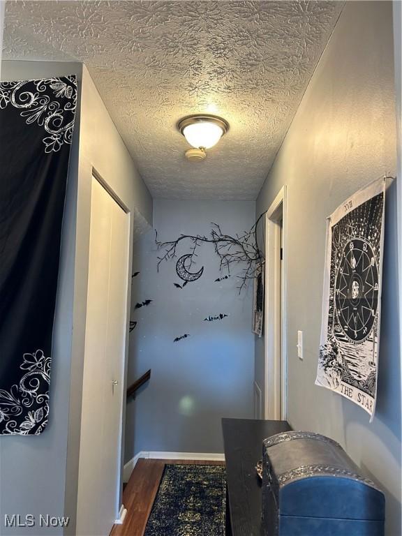 hallway with dark wood finished floors, baseboards, and a textured ceiling