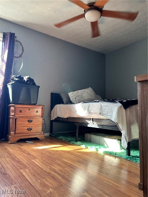 bedroom featuring a textured ceiling, a ceiling fan, and wood finished floors