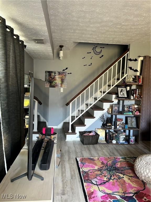 living room with visible vents, stairway, a textured ceiling, and wood finished floors