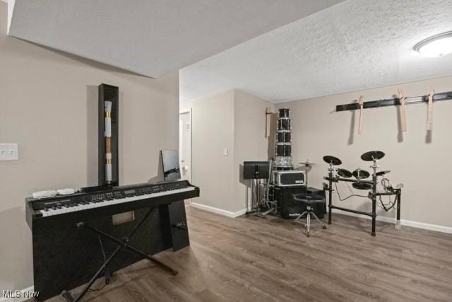 game room with baseboards, a textured ceiling, and wood finished floors