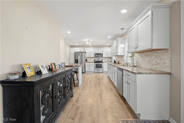 kitchen featuring light wood finished floors, backsplash, pendant lighting, appliances with stainless steel finishes, and a sink