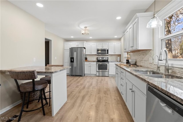 kitchen featuring a breakfast bar area, light stone countertops, a sink, decorative backsplash, and stainless steel appliances