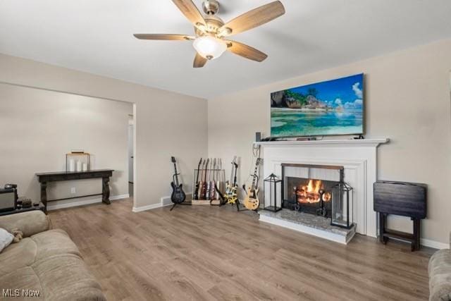 living room featuring a ceiling fan, wood finished floors, baseboards, and a lit fireplace