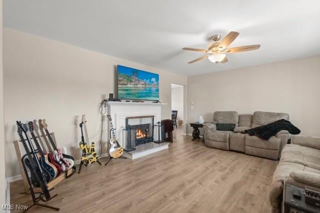 living room featuring a ceiling fan, wood finished floors, baseboards, and a warm lit fireplace